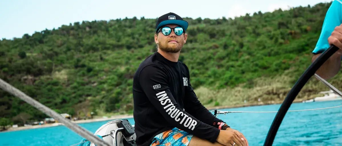 A Sailing Virgins instructor at the helm in a turquoise anchorage