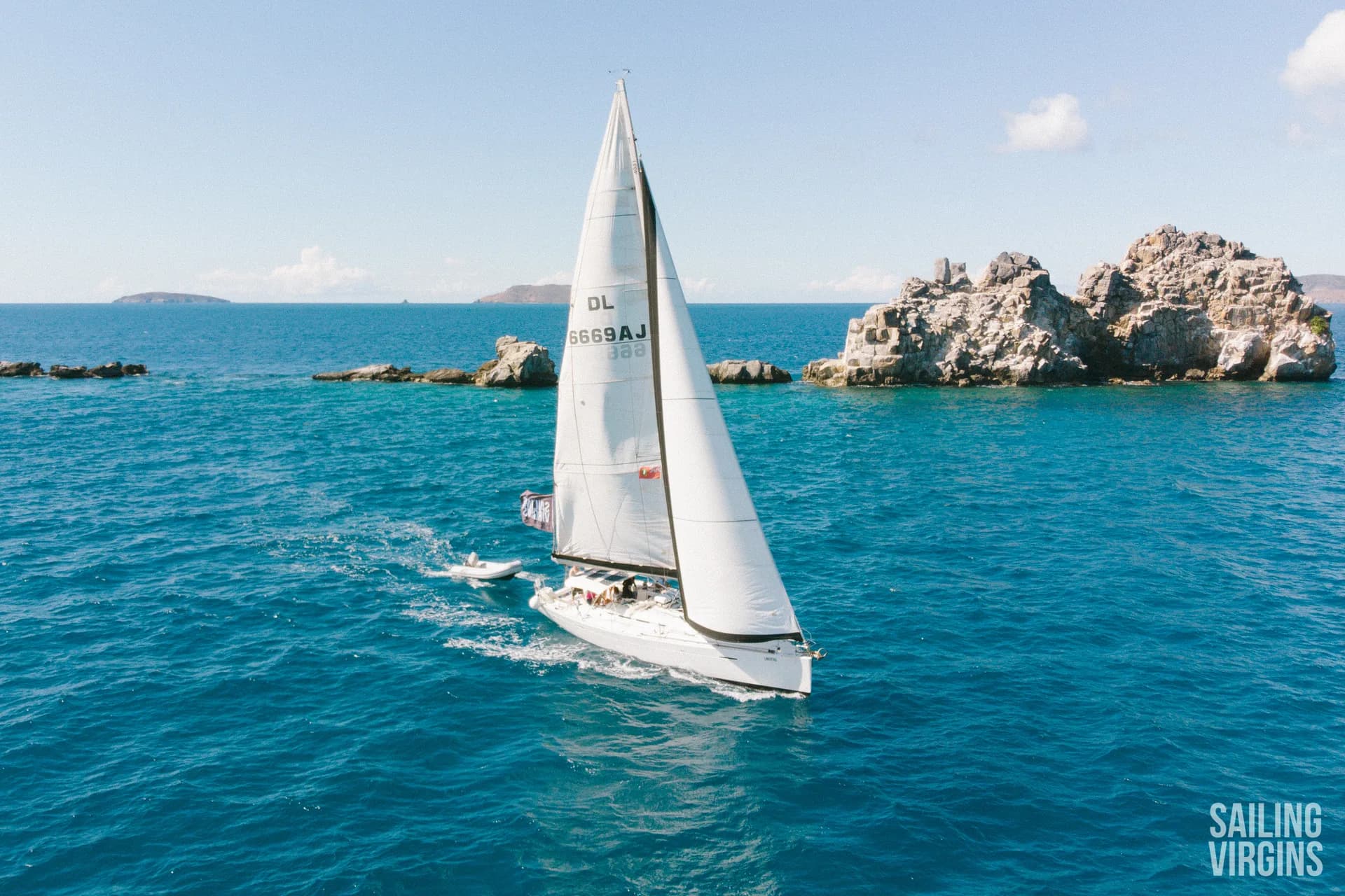 Aerial view of monohull sailing past rocks in the BVI