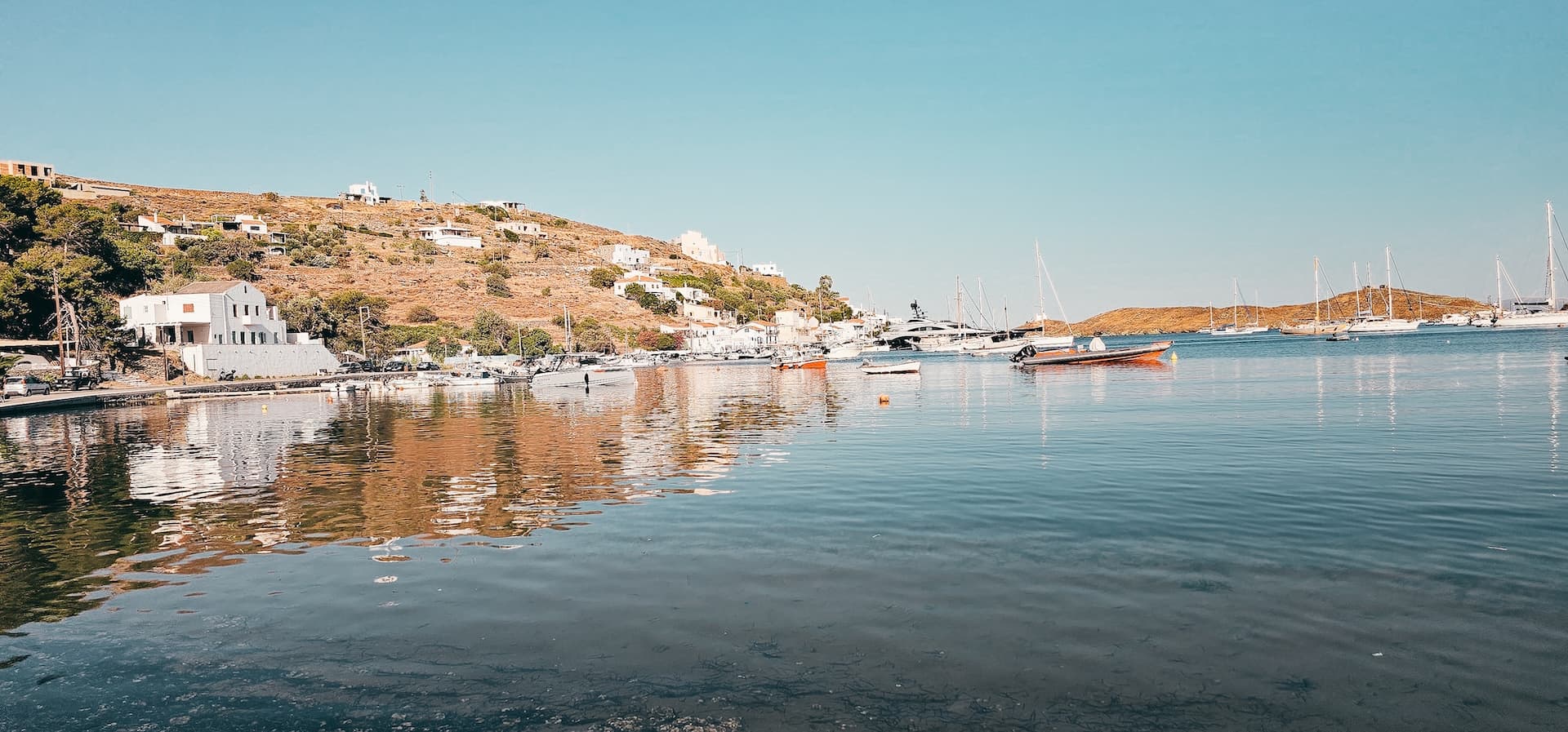 A Greek island harbour on a calm morning, white houses above the water and yachts at anchor
