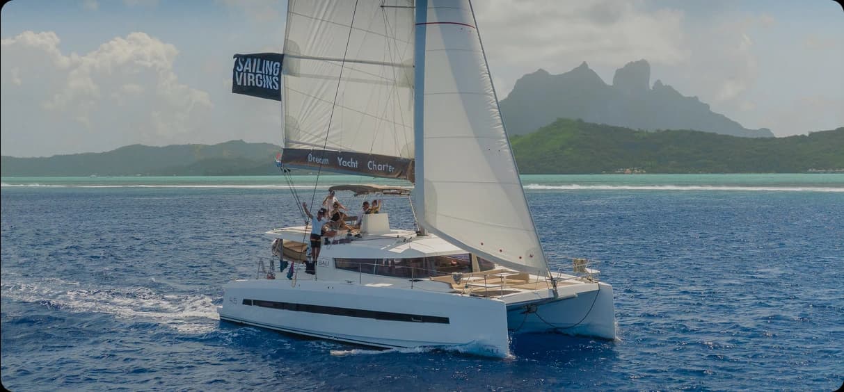 Elegant catamaran at sunset with champagne service on deck, turquoise water and distant islands in background