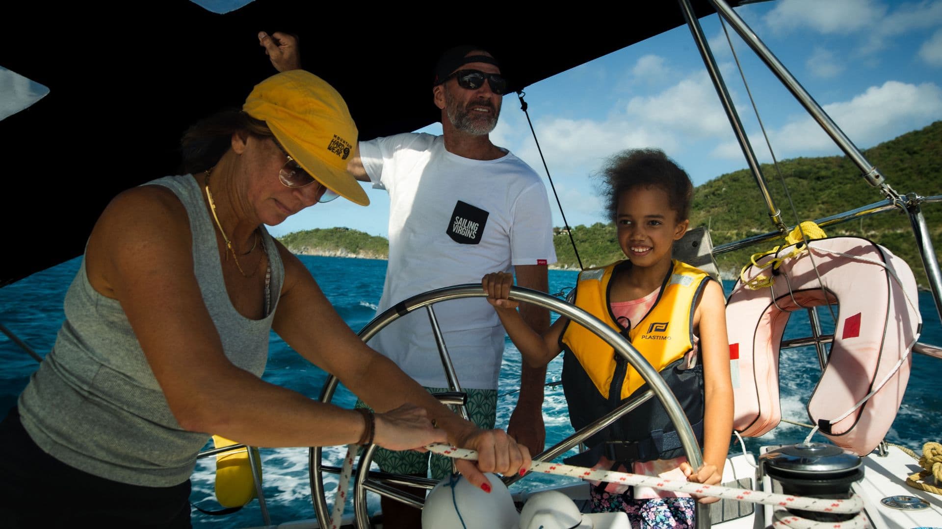 Happy family with two children sailing a catamaran together, parents teaching kids to steer while dolphins play in the wake